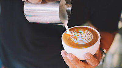 Schaum wird in eine Kaffeetasse gegossen, um Latte Art zu kreieren
