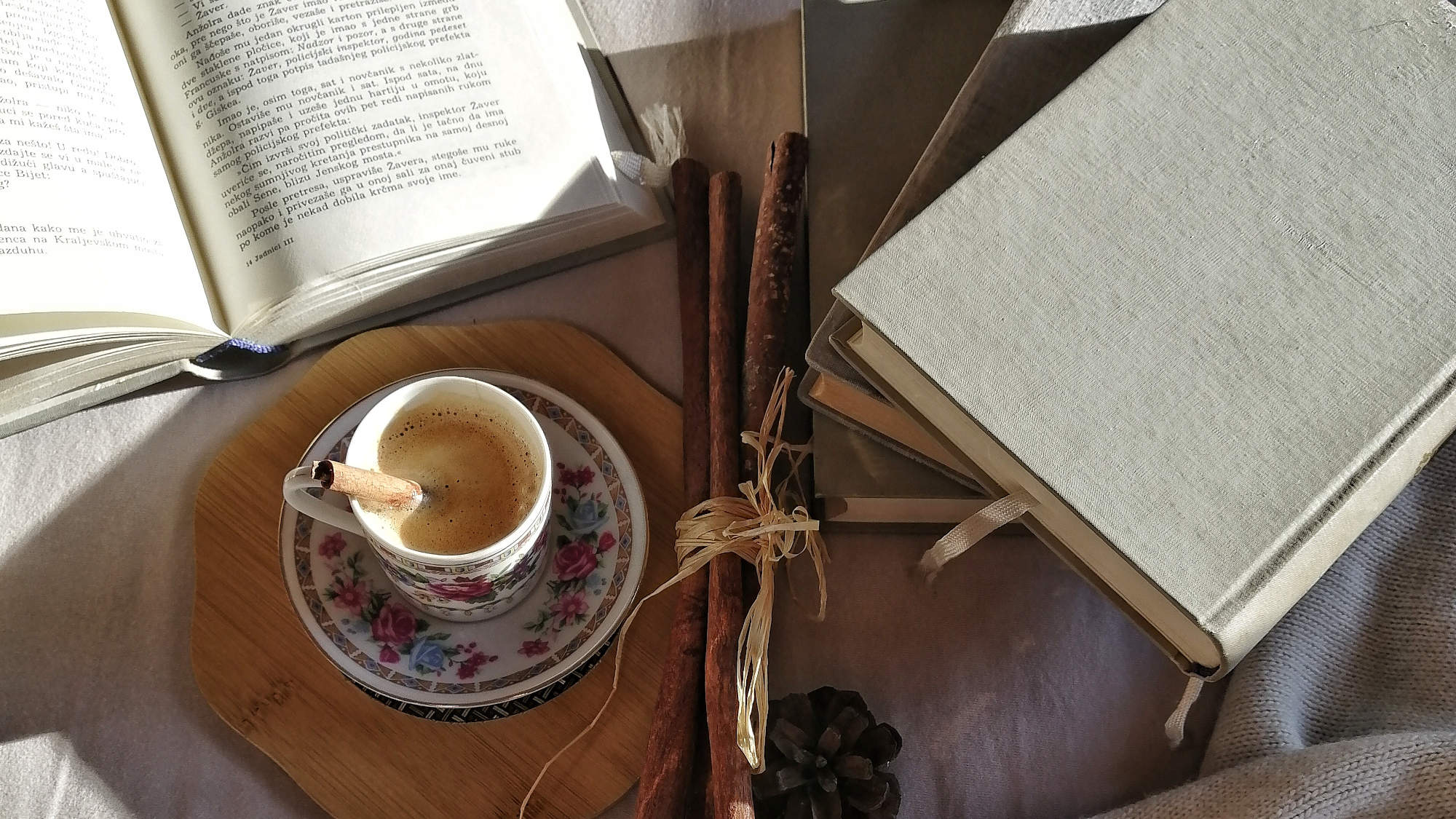 Ein Tisch mit einem offenen Buch, einigen geschlossenen Büchern auf einem Stapel, sowie einer Kaffeetasse darauf
