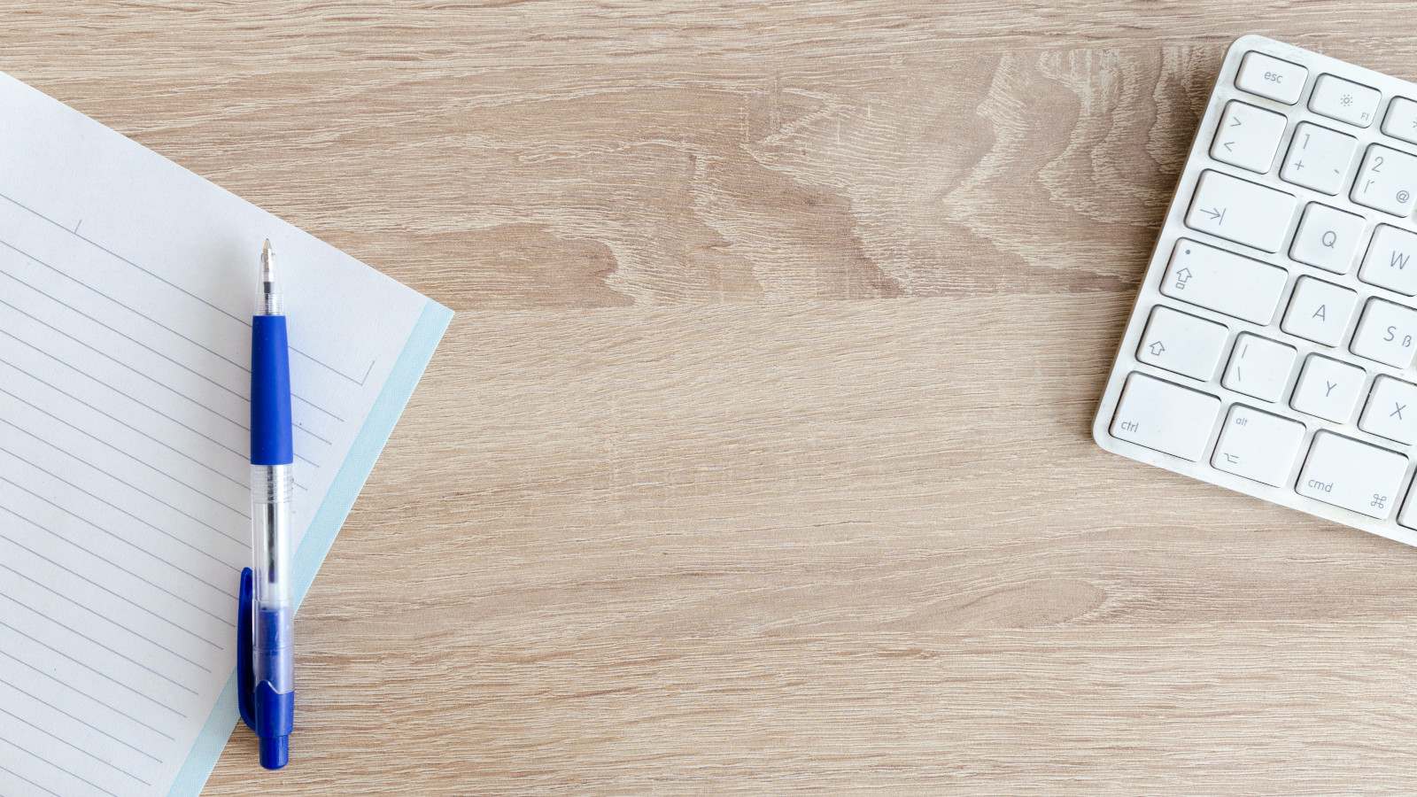 A wooden table with pen, paper and a keyboard