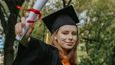Eine junge Frau die ein Diplom in Richtung Kamera hält