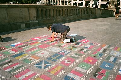 Ein Mann zeichnen Fahnen verschiedener Länder mit Kreide auf einen Gehsteig.